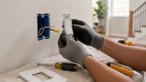 Gloved hands preparing a replacement light switch beside an open wall box